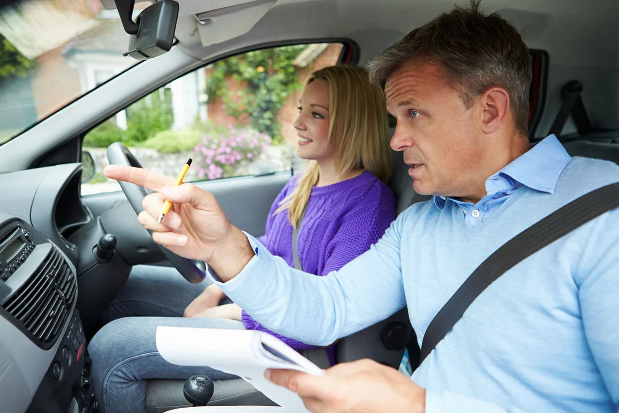 A driving instructor pointing out the road ahead to a learner at the wheel during a lesson
