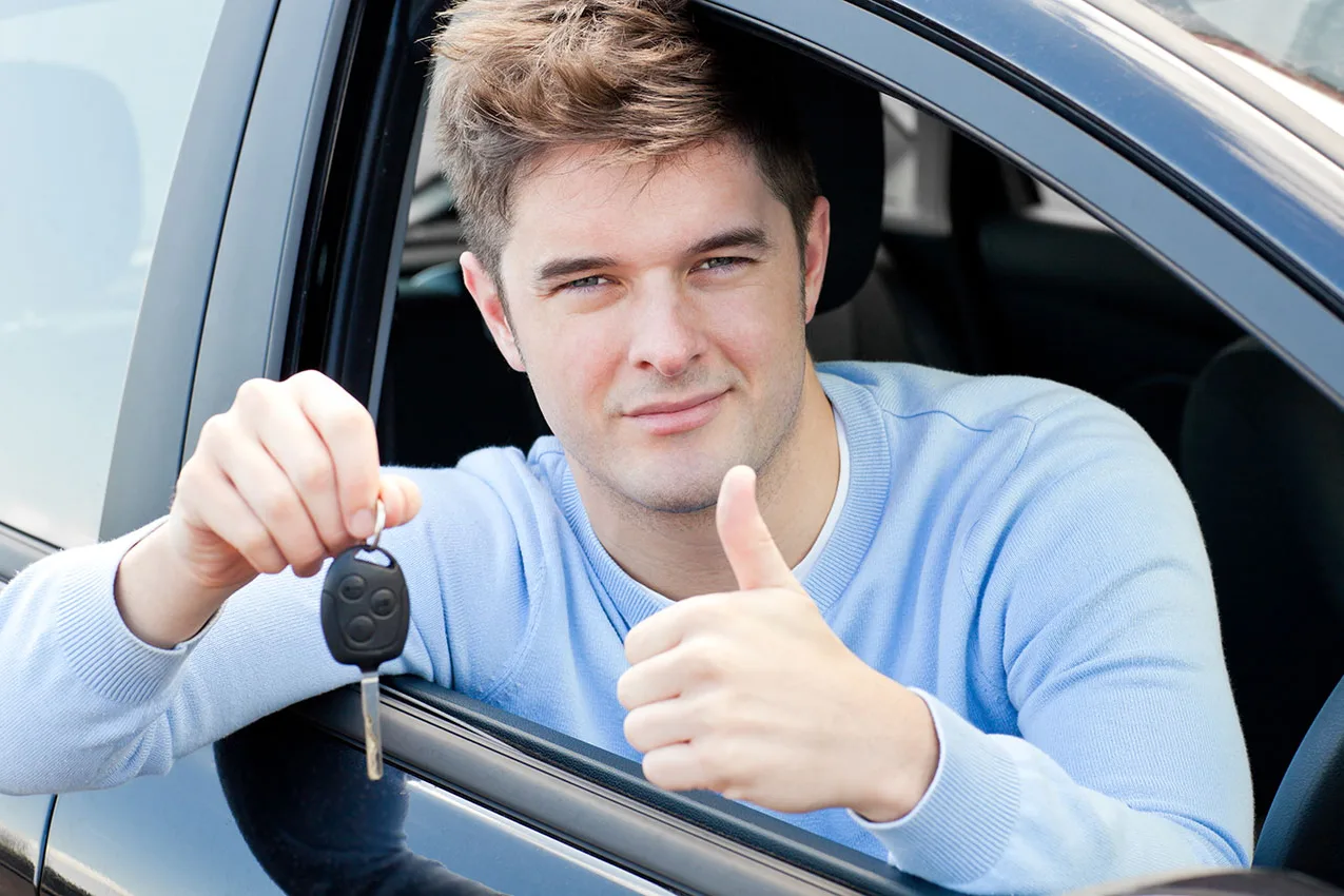 A new driver holding up a set of car keys and giving a thumbs up from the driver's seat