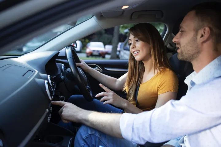 A driving instructor and a learner talking and smiling in the front of a car