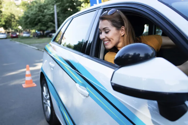 A learner leaning out of the car window during a manoeuvre, with a cone on the road behind