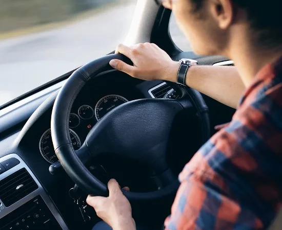A driver's hands on the steering wheel with the gear lever in view